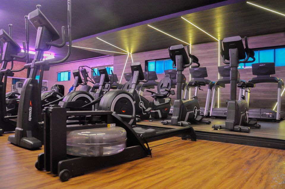 Sala de cardio da 349, com esteiras e elípticos enfileirados, piso de madeira e iluminação linear no teto.