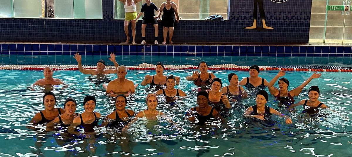 Turma de hidroginástica da 349 dentro da piscina, com os alunos sorrindo e alguns com as mãos levantadas.