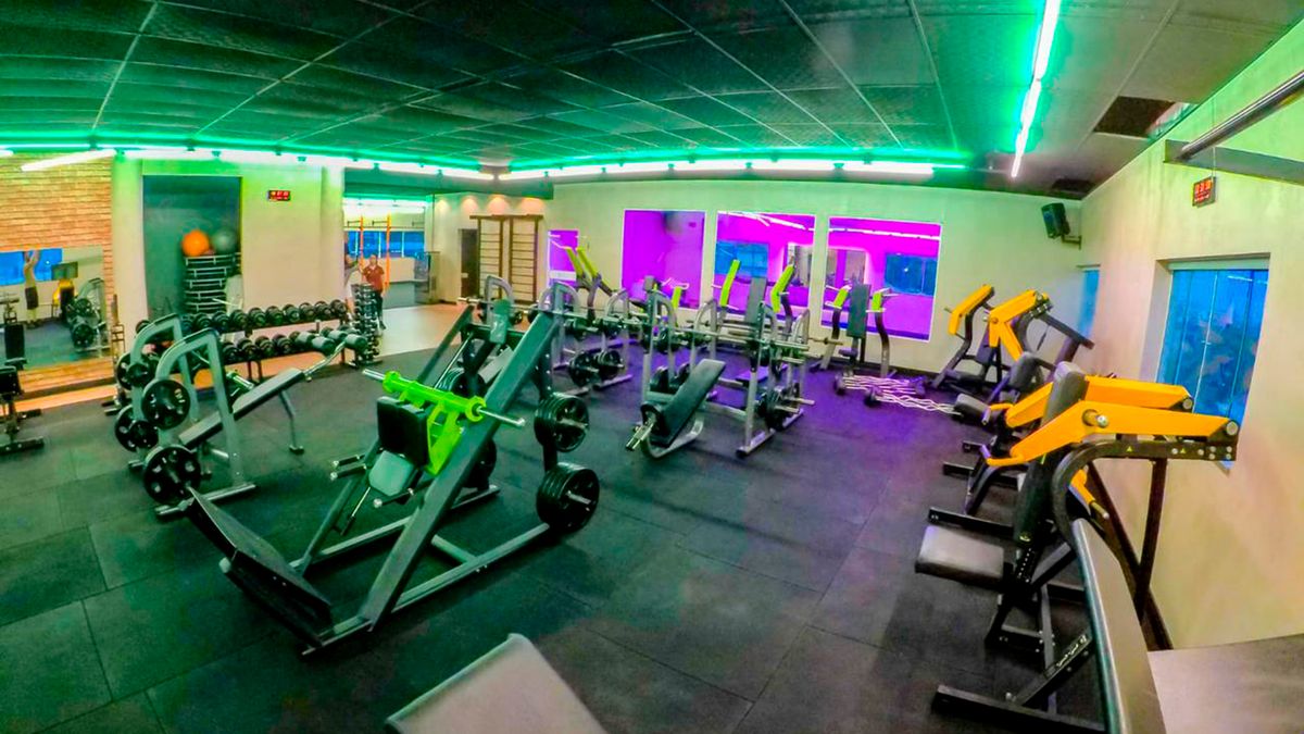 Sala de máquinas da 349 com iluminação em neon verde no teto e fileiras de aparelhos de musculação.